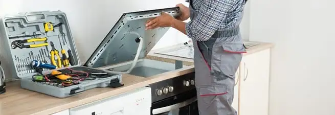 Cooktop repair technician lifting a built-in stovetop for service in West Palm Beach, FL
