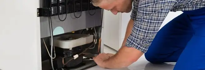 Refrigerator repair technician servicing the compressor and condenser area in West Palm Beach, FL