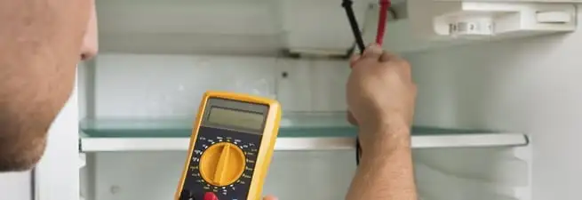Refrigerator repair technician testing electrical components with a multimeter in West Palm Beach, FL