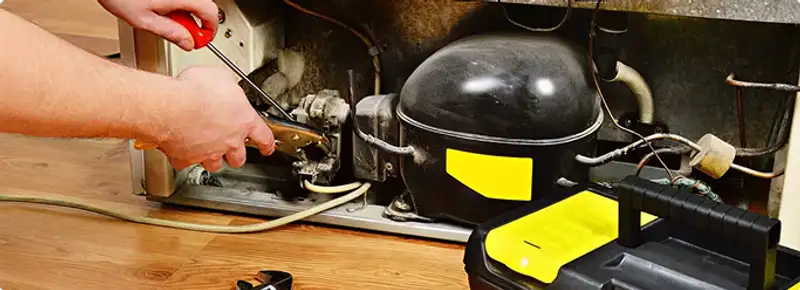 Refrigerator repair technician fixing the compressor and wiring in West Palm Beach, FL